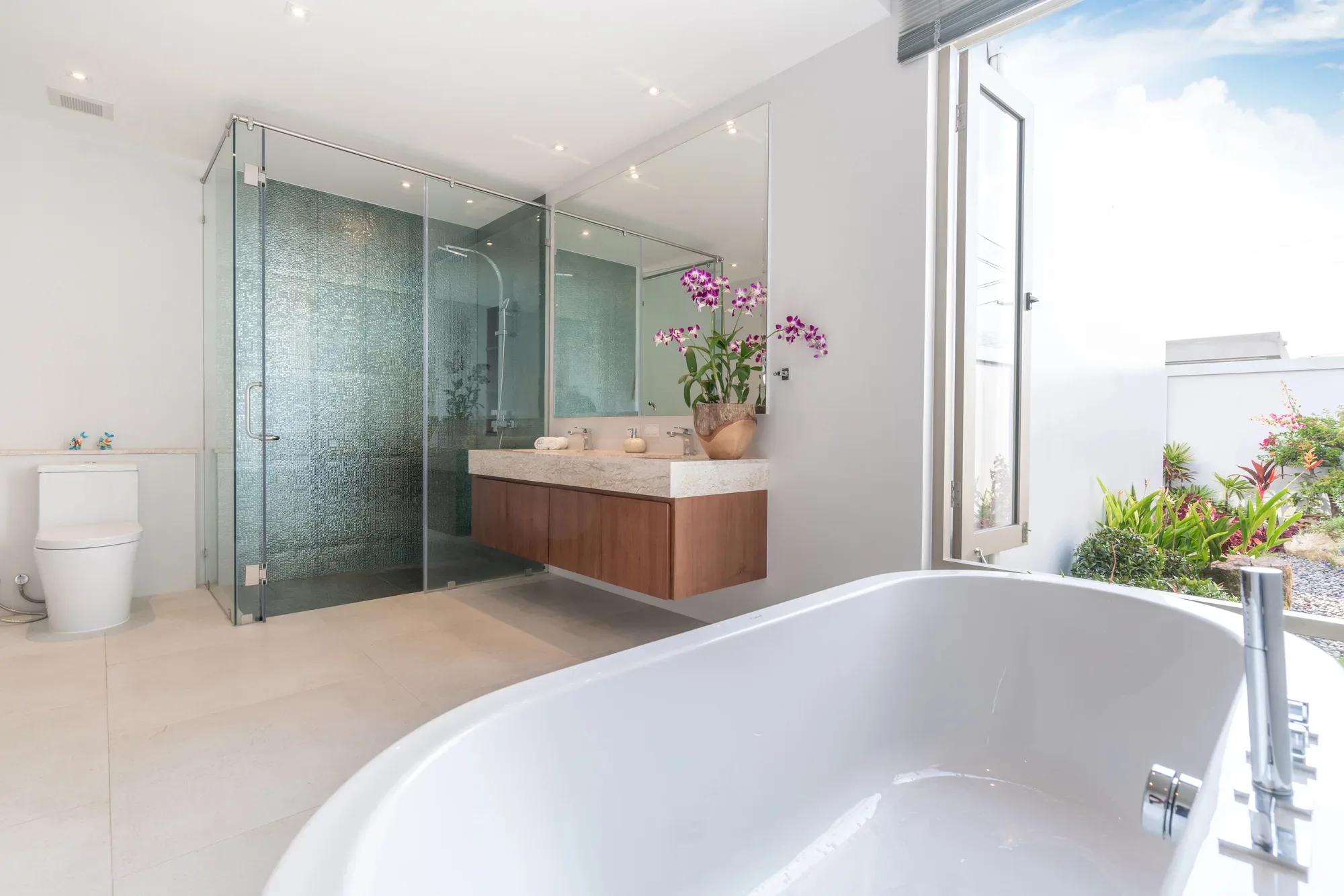 Modern glass-walled shower with timber vanity and garden view